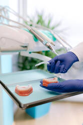 Von oben von einem nicht erkennbaren Kieferorthopäden in sterilen Handschuhen mit Kiefergipsen und durchsichtigen Zahnspangen in einer Klinik - ADSF38215