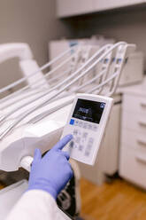 Unkenntlich gemachter Kieferorthopäde, der ein medizinisches Gerät mit Zahlen auf dem Display vor einer zahnärztlichen Einheit im Krankenhaus benutzt - ADSF38217