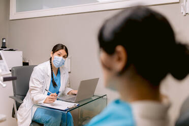 Kieferorthopädin mit Netbook und Papier im Gespräch mit einer anonymen Frau während einer zahnärztlichen Beratung in der Klinik - ADSF38221