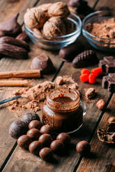 Various handmade chocolates with nuts arranged on wooden table with peanut butter and cinnamon sticks - ADSF38257