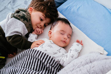 Von oben der charmante kleine Junge umarmt kleine Geschwister, während friedlich schlafen zusammen in gemütlichen Bett - ADSF38268