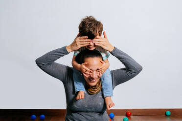 Little boy sitting on shoulders of excited mother and pretending to be plane while playing together at home - ADSF38278