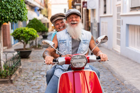 Front view of a modern senior couple riding on a motorcycle while driving through town - ADSF38283