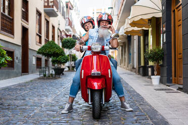 Blick von unten auf ein modernes älteres Paar mit Helmen auf einem roten Motorrad bei der Fahrt durch die Stadt - ADSF38291