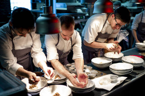 Junge Köche Männer in Schürzen sorgfältig servieren Mahlzeit in weißen Keramikschalen auf Restaurant Küche - ADSF38321