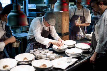 Junge Köche Männer in Schürzen sorgfältig servieren Mahlzeit in weißen Keramikschalen auf Restaurant Küche - ADSF38322