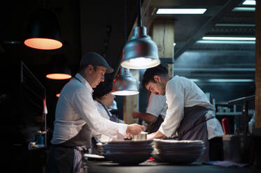 Junge Köche Männer in Schürzen sorgfältig servieren Mahlzeit in weißen Keramikschalen auf Restaurant Küche - ADSF38326