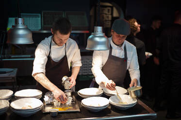 Junge Köche Männer in Schürzen sorgfältig servieren Mahlzeit in weißen Keramikschalen auf Restaurant Küche - ADSF38328