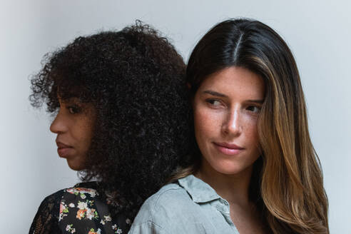 Young ethnic woman with Afro hairstyle in clothes with floral ornament standing close to female friend while looking away - ADSF38372