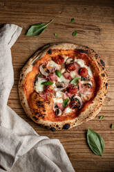 Draufsicht auf eine leckere Pizza mit Basilikum und Tomatensauce auf einem Holztisch in der Nähe einer Serviette in der Küche - ADSF38394
