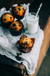 Leckere Muffins mit Schokoladenstückchen und einem Glas Milch auf dunklem Holzhintergrund - ADSF38411