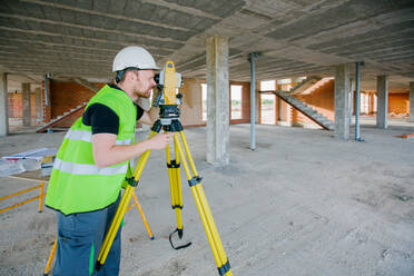 Vermessungsingenieur bei der Arbeit auf der Baustelle mit Messgeräten (Totalstation) - ADSF38431