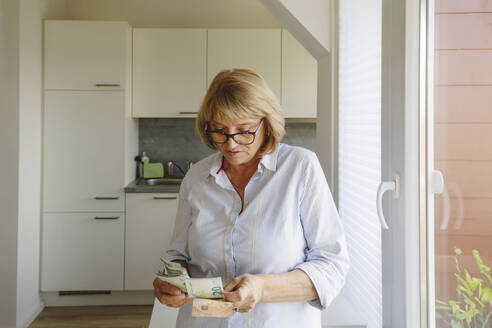 Ältere Frau mit Brille beim Zählen von Papiergeld zu Hause - IHF01268