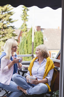Lächelnde Mutter und Tochter mit Kaffeetassen sitzen zusammen auf dem Balkon - IHF01286