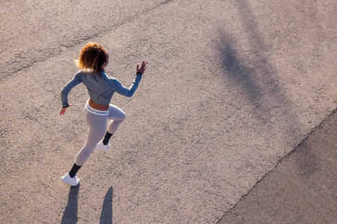 Von oben von einer entschlossenen Joggerin in Sportkleidung, die auf dem Bürgersteig und im Schatten im Sonnenlicht läuft - ADSF38451