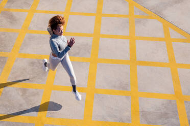 From above of determined female jogger in activewear running on pavement with ornament and shadow in sunlight - ADSF38452