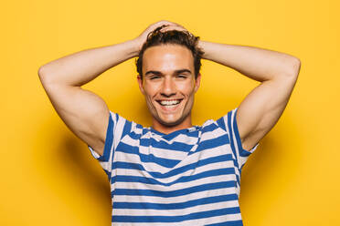 Junger cooler Mann in trendiger gestreifter Kleidung und zahnigem Lächeln, der mit halbgeöffneten Augen in die Kamera schaut, auf gelbem Hintergrund - ADSF38618