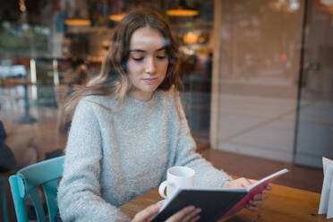 Junge Frau sitzt am Tisch in einem Café und genießt ein interessantes Buch, während sie einen schönen Tag genießt - ADSF38625