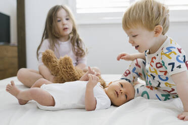 Brother and sister (2-3) with newborn boy (0-1 months) on bed - TETF01752