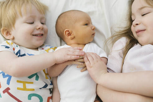 Bruder und Schwester (2-3) mit neugeborenem Jungen (0-1 Monate) im Bett - TETF01753