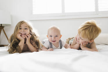 Portrait of siblings (6-11 months, 2-3) lying on bed - TETF01796