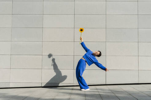 Happy woman with sunflower bending over backwards by wall - SEAF01212