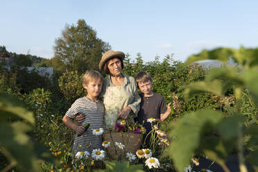 Senior woman with grandchildren standing amidst plants in flower garden - VBUF00165