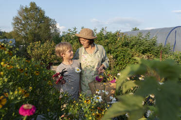 Smiling senior woman wearing hat standing with grandson in garden - VBUF00166