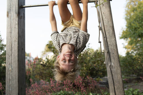 Happy blond boy hanging upside down on horizontal bar - VBUF00173