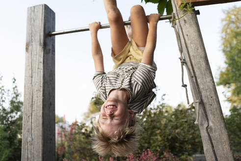 Cheerful boy hanging upside down on horizontal bar - VBUF00175