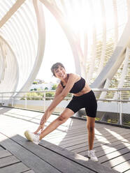 Happy athlete practicing stretching exercise on footpath - AMRF00008