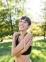 Happy young athlete hugging self in park - AMRF00024