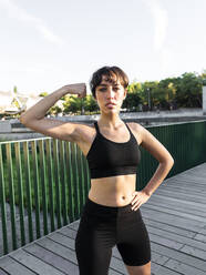 Junge Sportlerin beim Muskeltraining vor einem Geländer auf einer Brücke stehend - AMRF00027