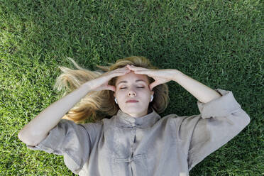 Frau mit geschlossenen Augen reibt sich den Kopf, indem sie im Gras liegt - TYF00415
