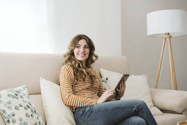 Lächelnde junge Frau mit digitalem Tablet auf dem Sofa zu Hause - EBBF06407