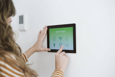 Nahaufnahme einer Frau, die ein digitales Tablet mit einer Smart-Home-App an der Wand benutzt - EBBF06415