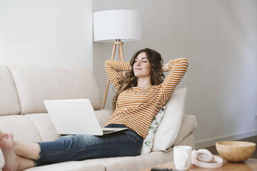 Young woman with laptop relaxing on sofa at home - EBBF06432