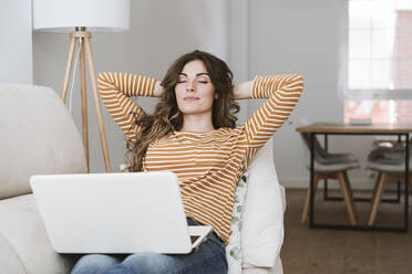 Young woman with laptop relaxing on sofa at home - EBBF06433