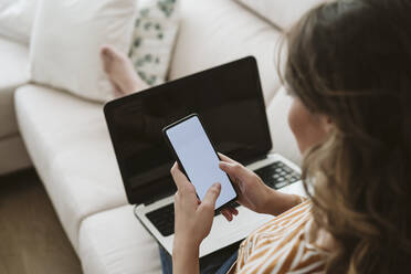 Frau mit Laptop und Mobiltelefon auf dem Sofa - EBBF06434