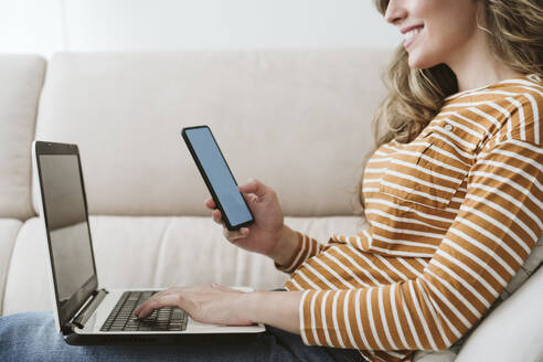 Frau mit Laptop und Mobiltelefon auf dem Sofa - EBBF06435