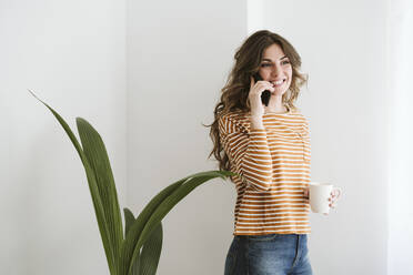 Lächelnde junge Frau am Telefon mit Kaffeetasse - EBBF06446