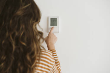 Woman adjusting heating control on the wall - EBBF06447