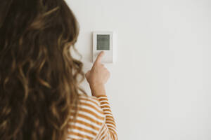 Frau stellt den Heizungsregler an der Wand ein - EBBF06447