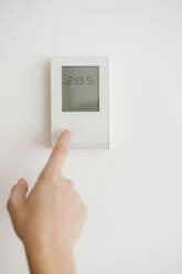 Finger touching thermostat on the wall - EBBF06448