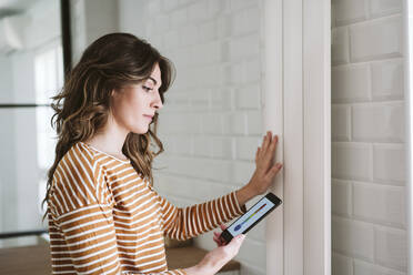 Young woman using smart phone app and touching radiator at home - EBBF06474