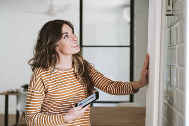 Young woman using smart phone app and touching radiator at home - EBBF06477