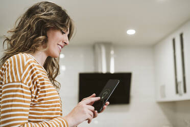 Junge Frau, die ein Mobiltelefon mit einer Smart-Home-App für die Beleuchtung zu Hause benutzt - EBBF06484
