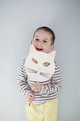 Happy cute boy standing with handmade Halloween mask in front of gray wall - ONAF00002