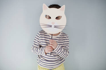 Boy hiding face behind animal mask in front of wall - ONAF00003