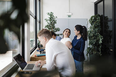 Glückliche Geschäftsfrau mit Kollegen, die im Büro am Laptop arbeiten - DCRF01356